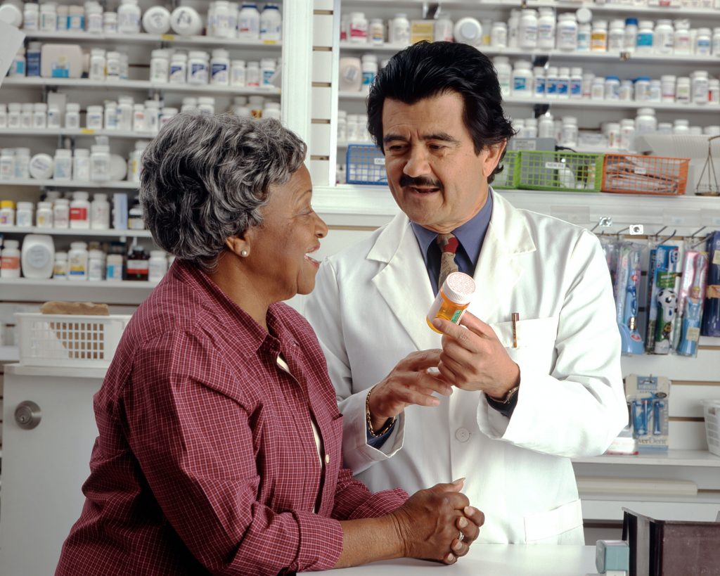 An Asian male Pharmacist discusses information on a bottle of medicine with an older Black woman