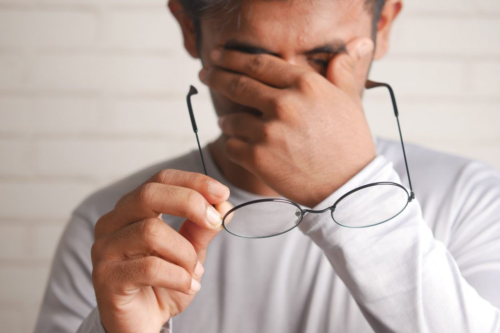 A man holds his glasses in front of his face while rubbing his eyes in tiredness with his other hand. Photo by Towfiqu barbhuiya on Unsplash.com